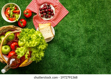 Picnic Setting On Meadow With Basket And Food On Red Cloth. Overhead View