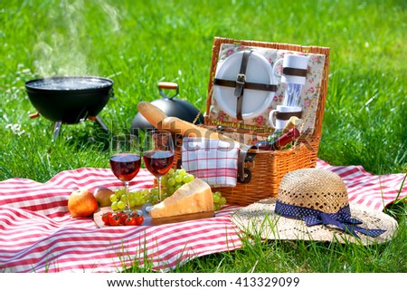 Picnic setting with red wine glasses, basket and burning fire in a portable barbecue