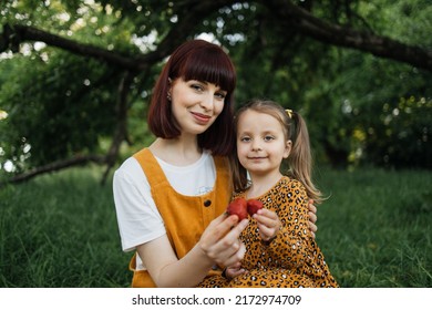 Picnic In Summer Park. Close Up Portrait Of Single Mom With Little Daughter Is Engaged In Eating Strawberry Resting Outdoor.