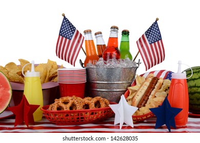 A picnic table set up with a Fourth of July theme. Horizontal format with a white background. Items include a soda bucket, hot dog, watermelon, chips, pretzels, and American Flag accessories. - Powered by Shutterstock