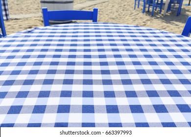 Picnic Table With White And Blue Table Cloth By The Sea In Greece, Empty Picnic Table For Product Display, De Focused Beach In The Background