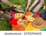 Picnic time, girls eating food on a colorful blanket, cooler bag on grass at summer park. Sandwiches with egg and tuna, pie with rice and meat, vegetables and cookies.