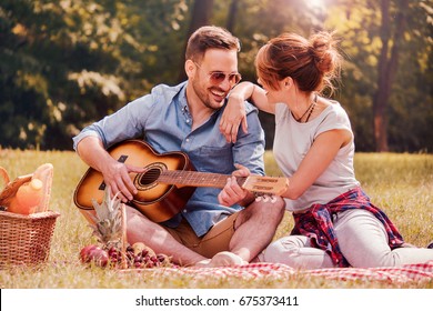 Picnic time. Young couple having fun with guitar on picnic in the park. Love and tenderness, dating, romance, lifestyle concept