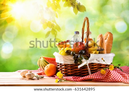 Picnic wicker basket with food on table in the field with green nature background. Picnic concept. Front view. Horizontal composition.