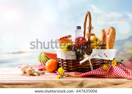 Picnic wicker basket with food on wood table on the beach with blue sky background and sun. Picnic concept. Front view. Horizontal composition.