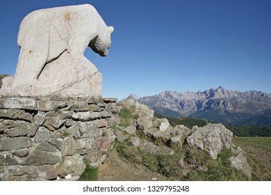 Picos De Europa. Spain . June. Large Statue Of A Bear Carved From White Stone. On A Rock Plinth And Looking Towards The Distant Mountain Range. Blue Sky, No Snow.