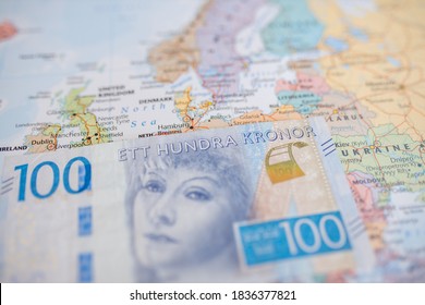 Picture of a 100 Swedish Kronor Banknote (with the words One Hundred Kronor in Swedish) on Top of a blurry and colorful European Map, showing the Face of Greta Garbo