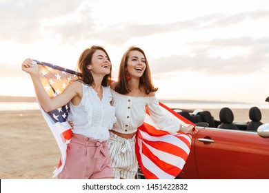 Picture of amazing young happy smiling cheery women friends walking near car outdoors at the beach holding USA flag. - Powered by Shutterstock