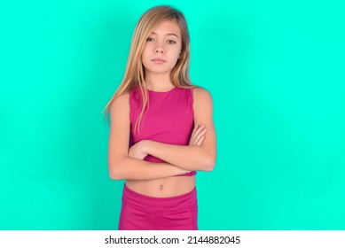 Picture Of Angry Blonde Little Kid Girl Wearing Pink Sport Clothes Over Green Background Looking Camera.