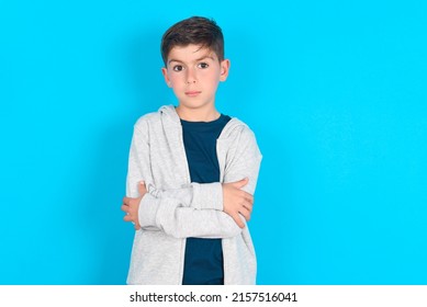 Picture Of Angry Caucasian Kid Boy Wearing Grey Hoodie Over Blue Background Looking Camera.