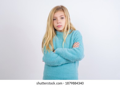 Picture Of Angry Cute Caucasian Kid Girl Wearing Blue Knitted Sweater Against White Wall Looking Camera.