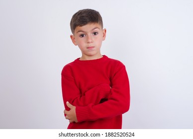 Picture Of Angry Cute Caucasian Kid Boy Wearing Knitted Sweater Against White Wall Looking Camera.