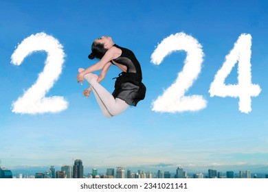 Picture of Asian ballerina jumping with clouds shaped number 2024 with cityscape background - Powered by Shutterstock