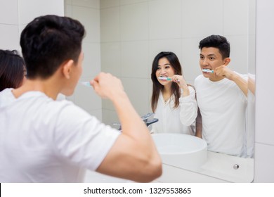 Picture Of Asian Couple Brushing Teeth In The Bathroom While Looking At Mirror