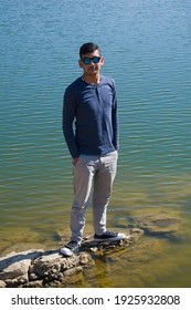 Picture Of Asian Indian Ethnicity Boy Standing On Lake Shore Wearing Blue Shirt And Sunglasses.