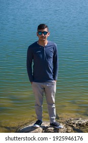 Picture Of Asian Indian Ethnicity Boy Standing On Lake Shore Wearing Blue Shirt And Sunglasses.