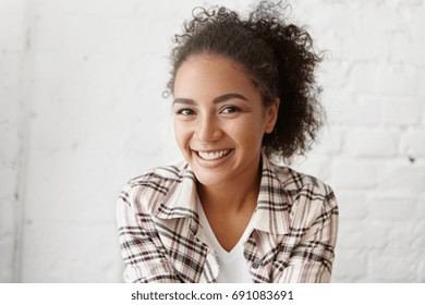 Picture Of Beautiful Mixed-race College Girl With Afro Hairstyle Smiling Broadly, Showing Her White Straight Teeth At Camera, Rejoicing At Good News Or Nice Day, Relaxing At Cafe After University