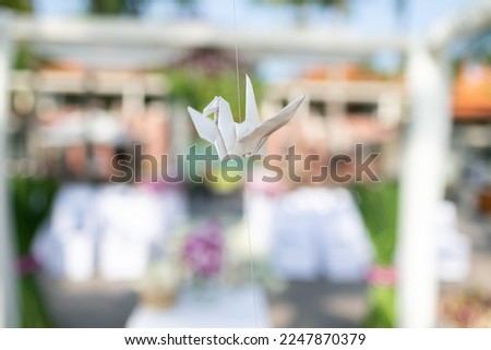 A picture of a bird folded with white paper and hung on a sling in a wedding ceremony. Representing independence, freedom, flying, being one, looking at it and feeling creative