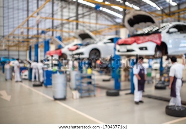 The picture is blurry while the mechanic works\
in the car service center. There are cars. Many customers come to\
use the oil change service.