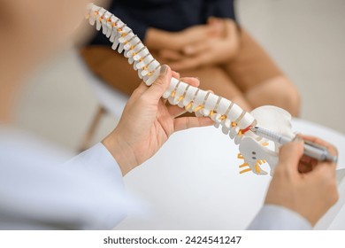 Picture of a close-up of an orthopedic doctor pointing at a spinal model and explaining to a female patient her spinal problems. Health care concept and aging and back pain - Powered by Shutterstock