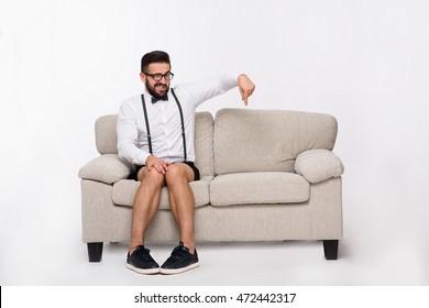 Picture of confident  handsome hipster man pointing down while sitting on sofa or couch isolated on white background in studio. Studio shot. Emotions concept. - Shutterstock ID 472442317
