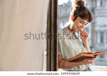 Picture of a cute happy young beautiful woman reading book on a balcony.