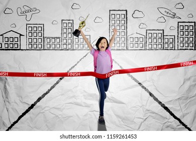 Picture of cute schoolgirl carrying a trophy while crossing the finish line. Shot with crumpled background  - Powered by Shutterstock