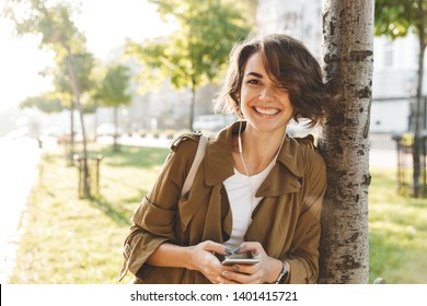 Picture Of A Cute Young Pretty Woman Walking Outdoors In Park In Beautiful Spring Day Using Mobile Phone.