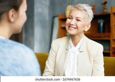 Picture Of Elegant Sixty Year Old Female Psychological Counselor With Stylish Haircut Providing Counseling Assistance To Her Female Client, Sitting In Armchairs In Front Of Each Other, Talking