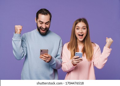 Picture of excited surprised loving couple isolated over purple background using mobile phones make winner gesture. - Shutterstock ID 1704476518