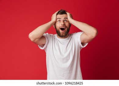 Picture of excited young handsome man standing isolated over red wall background. Looking aside. - Shutterstock ID 1096218425