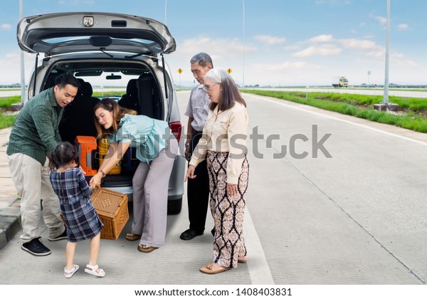 Picture\
of extended family ready for a road trip while preparing suitcase\
into a car for holiday and standing on the\
road