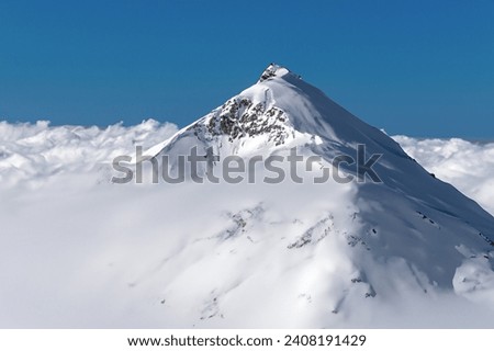 The picture features a majestic snowy mountain peak set against a clear blue sky. Its pristine white slopes stand in stark contrast to the vibrant azure backdrop, creating a breathtaking vista.