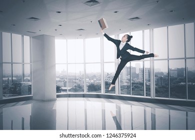 Picture of female entrepreneur reading a book and jumping near the window. Shot in the office - Powered by Shutterstock