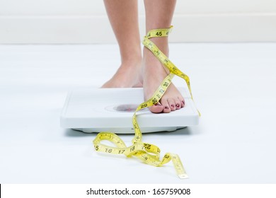 A picture of female feet standing on a bathroom scales and a tape measure 