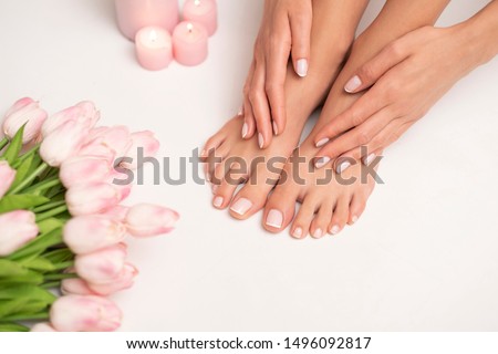 The picture of female legs and hands after pedicure and manicure. Legs are surrounded by pink tulips and candles.