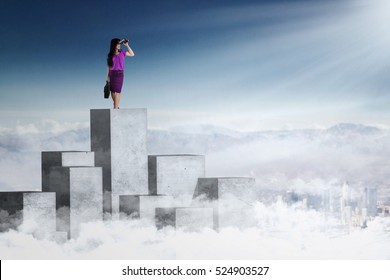 Picture of a female worker standing on the concrete wall and using binoculars to look at sky