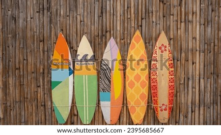 A picture of five surfboards resting against a brown bamboo wall. Each surfboard has different colors, patterns, and sizes.