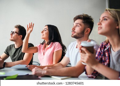 Picture Of Four People Sitting Together In One Room. Brunette Hold One Hand Up. They Study. Blonde Model Hold Up Of Coffee.