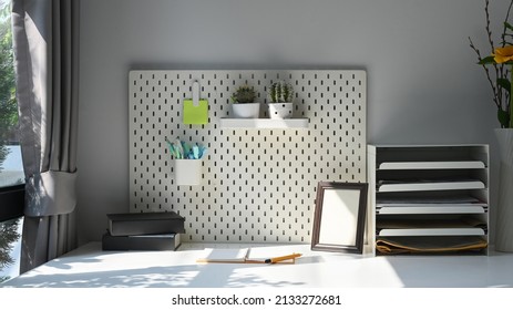 Picture Frame, Supplies, Houseplant And Pegboard On White Table In Home Office.