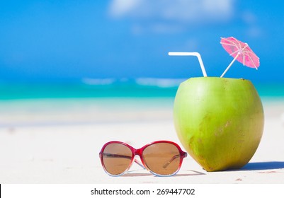 picture of fresh coconut cocktail and blue sunglasses on tropical beach