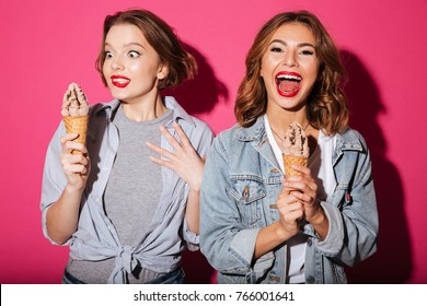 Picture Of Funny Two Women Friends Standing Isolated Over Pink Background Eating Ice Cream.