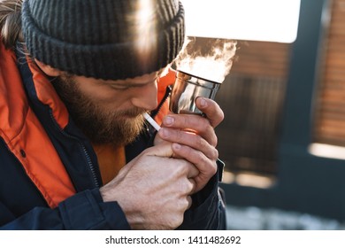 Picture of a handsome young man fisherman wearing coat and hat at the seashore smoking. - Shutterstock ID 1411482692