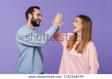 Picture of happy cheery optimistic loving couple posing isolated over purple background giving high five.