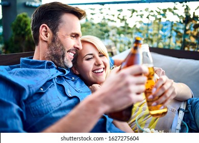 Picture of happy couple resting on patio together during summer day with beer and popcorn - Powered by Shutterstock