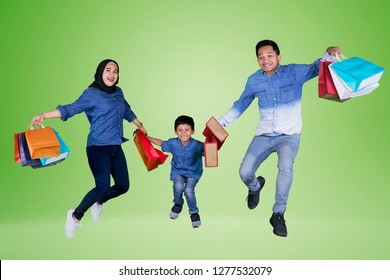 Picture Of Happy Family Holding Shopping Bags While Jumping Together In The Studio, Shot With Green Screen