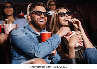 Picture of happy friends sitting in cinema watch film eating popcorn and drinking aerated sweet water.