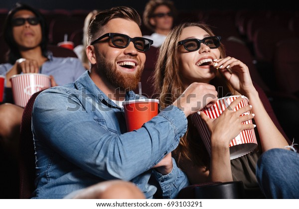 Picture of happy friends\
sitting in cinema watch film eating popcorn and drinking aerated\
sweet water.