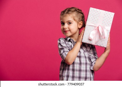 Picture Of Happy Little Girl Child Standing Isolated Over Pink Background. Looking Camera Holding Gift Box Surprise.