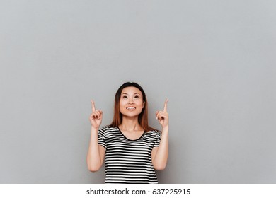 Bild einer glücklichen jungen asiatischen Frau, die über einer grauen Wand steht. Blick zur Seite.